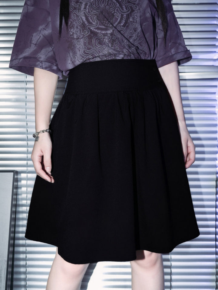 A full-length view of a model showcasing a black dark academia midi skirt with a thick high waistband and gathered pleats, styled with a purple cyber grunge top and a silver metallic hardware belt.