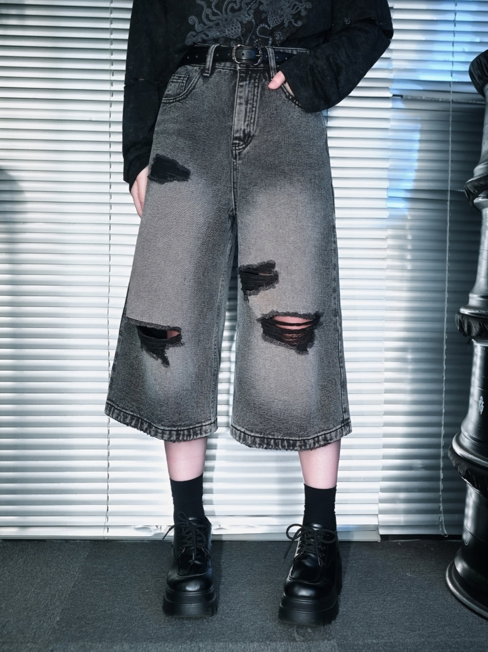 A close-up and full-length view of a model styling loose grey cyber grunge denim shorts featuring heavy shredded knee cutouts, paired with a washed black graphic tee and platform creepers.