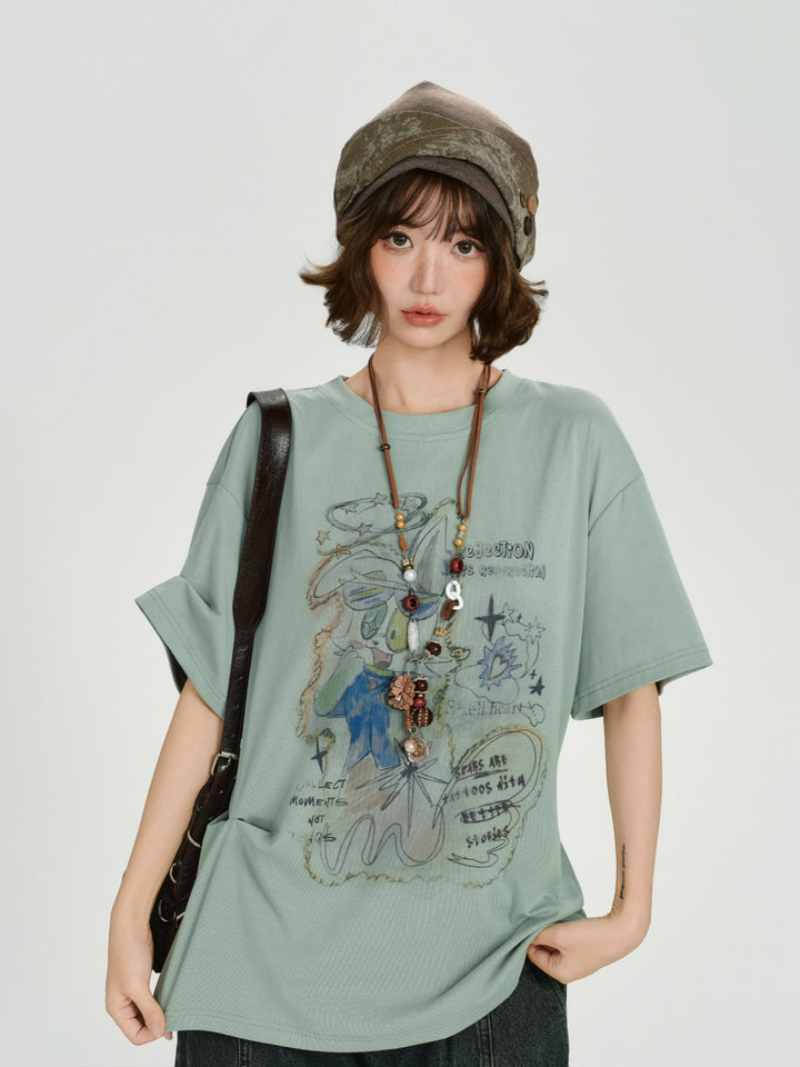 Oversized sage green t-shirt featuring a vintage hand-drawn cartoon graphic with whimsical doodles and artistic text.