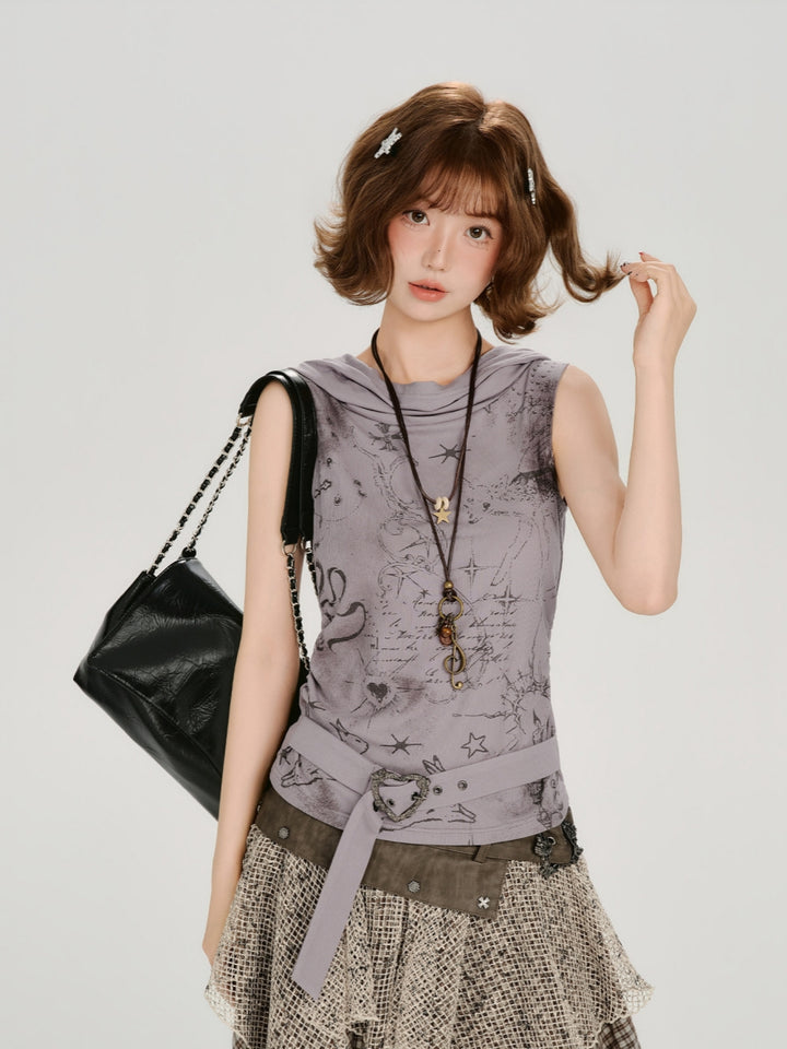 A model poses in a fairy-grunge aesthetic sleeveless hooded top featuring faded black celestial and star graphics on a muted purple fabric. The top has a unique cowl neck hood and is accessorized with a heart-buckle belt and layered earthy necklaces. She is paired with a distressed mesh layered skirt for a complete wasteland aesthetic.