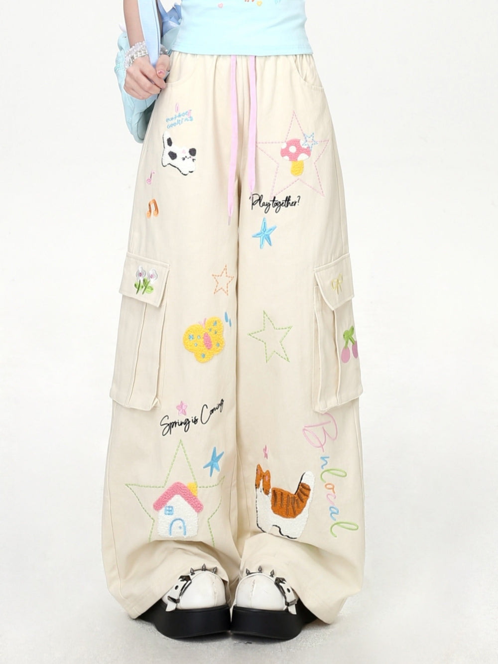 Model wearing cream and black Cyber Y2K kawaii baggy cargo pants with colorful cartoon character embroidery.