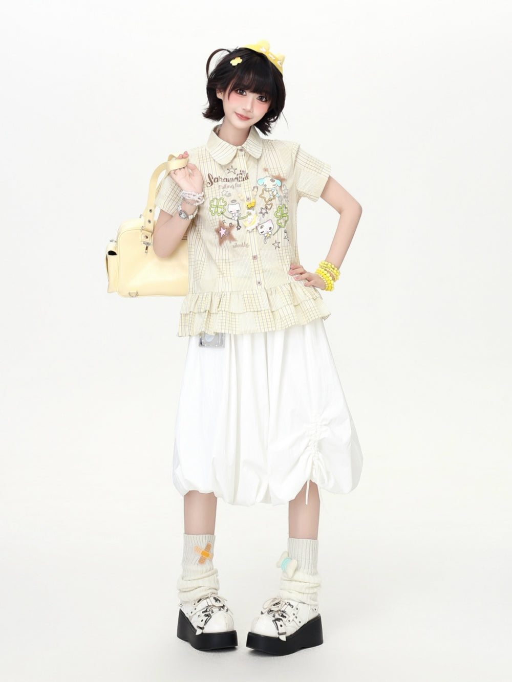 Model wearing a pastel yellow and lavender Cyber Y2K plaid short sleeve shirt with cartoon graphics and tiered ruffle hem detail.