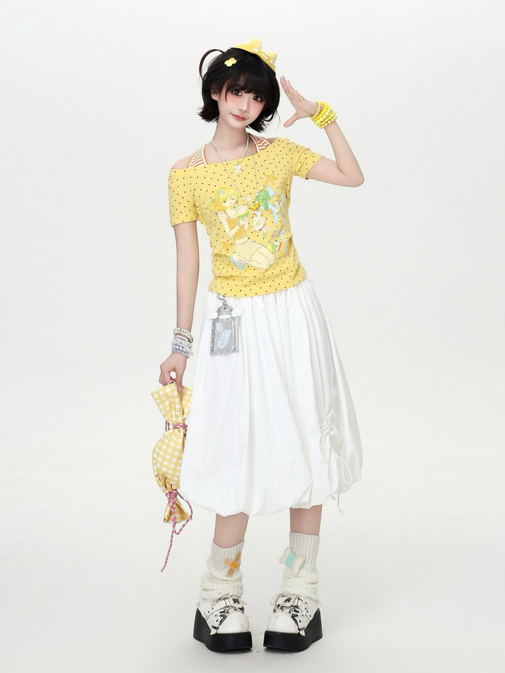 Model wearing a yellow and white polka dot Cyber Y2K kawaii graphic crop top with built-in striped halter straps and a retro anime character print.