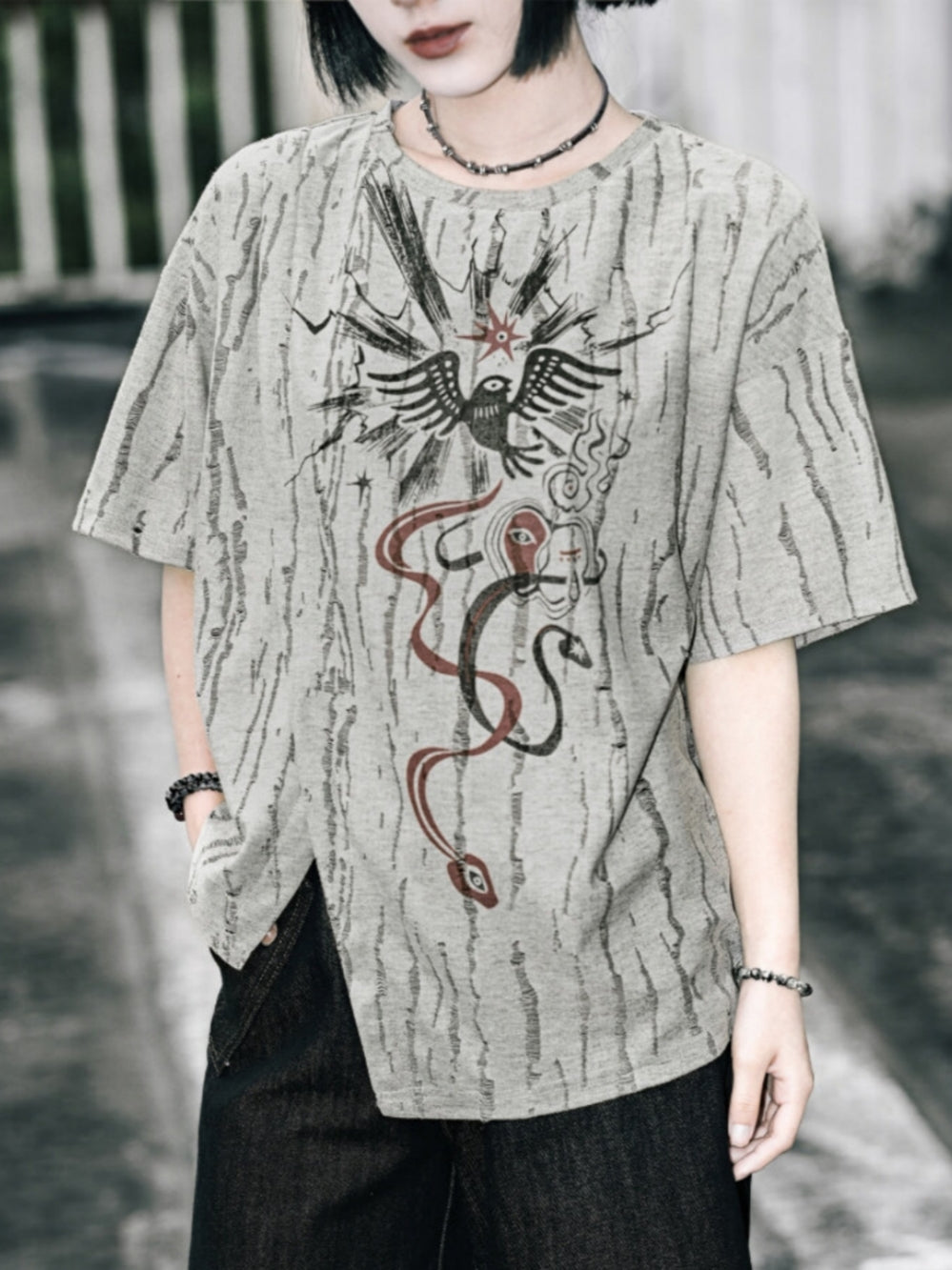 A model wearing a grey cyber grunge graphic tee featuring a unique bark-like textured fabric, a black raven and snake occult print on the front, and an asymmetric side slit at the hem.