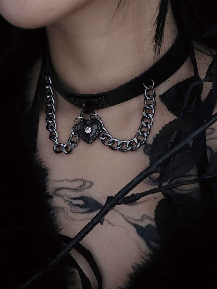 Black choker with a central heart-shaped padlock pendant, a clear sparkling accent, and chains draped in loops on either side.
