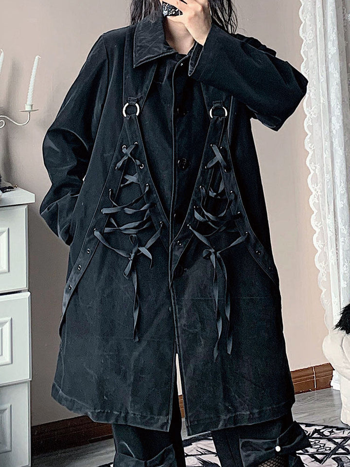 Black oversized long coat with a pointed collar and ring-connected straps framing two crisscross-laced panels on either side of the front buttons.