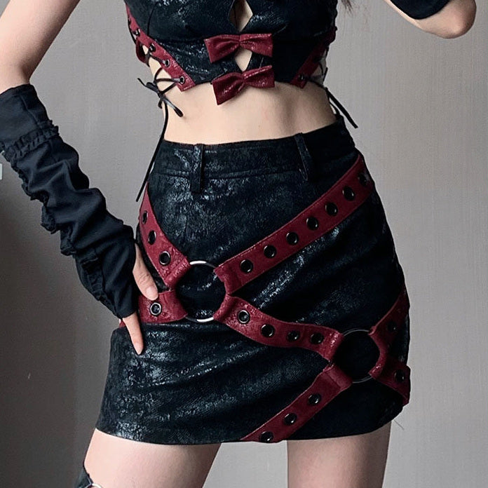 Burgundy grommet straps run diagonally across a black punk mini skirt, joining at two large rings on the front.
