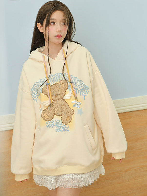 Oversized cream pastel hoodie featuring a cute teddy bear graphic with angel wings and colorful drawstrings, styled with a lace ruffle skirt.