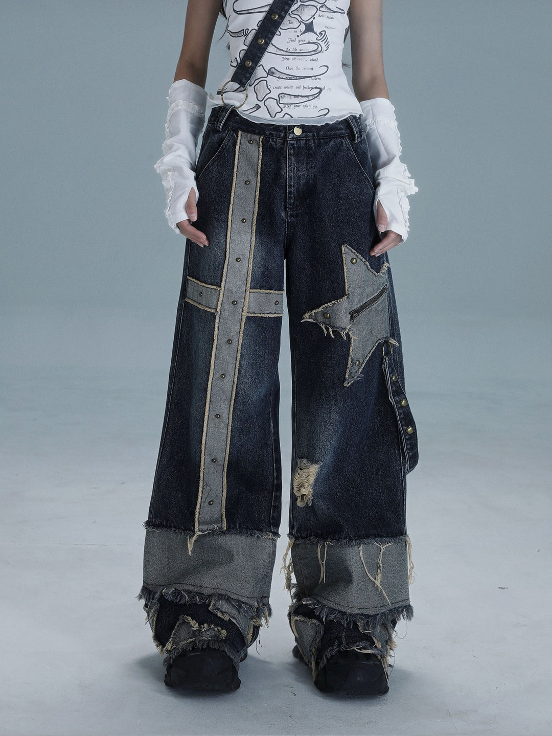 Dark wide-leg punk patchwork jeans with a long studded cross panel on one leg, a zippered star patch on the other and heavily frayed contrasting cuffs.