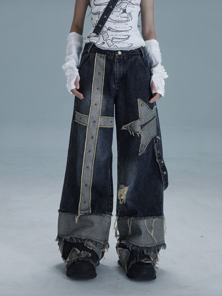Dark wide-leg punk patchwork jeans with a long studded cross panel on one leg, a zippered star patch on the other and heavily frayed contrasting cuffs.