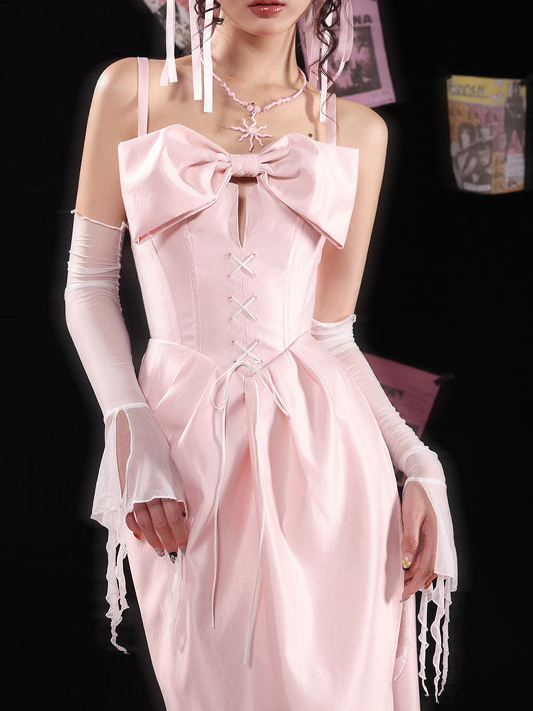 Pink midi dress with slim shoulder straps, a large bow above a chest cutout and white lacing down the fitted bodice, opening into a pleated skirt with a front slit.