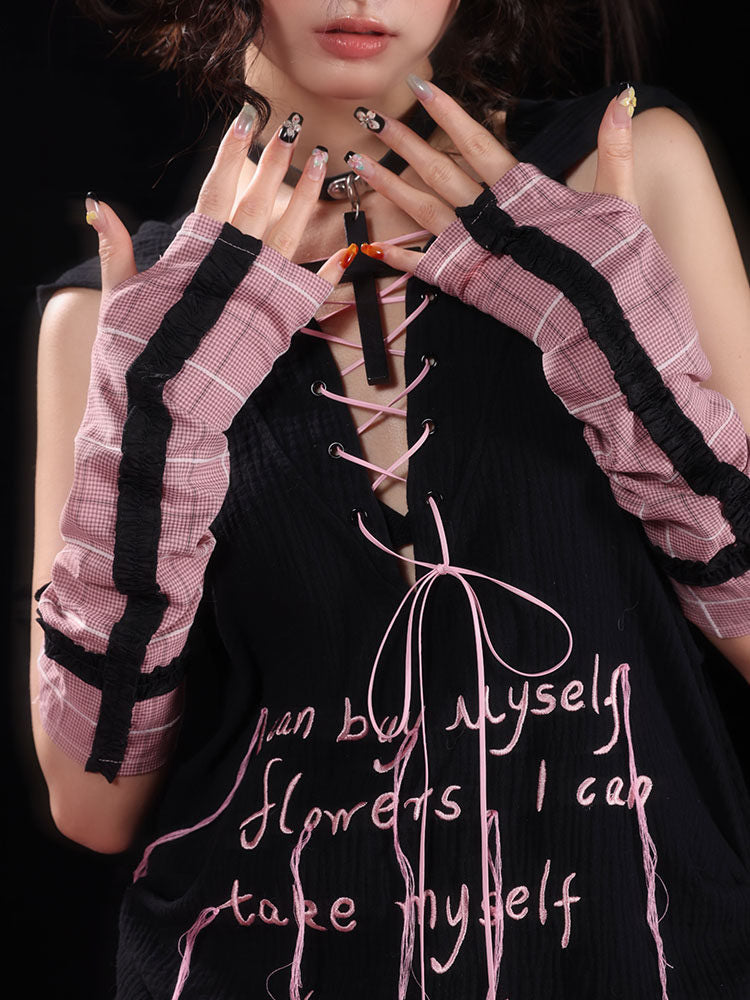 Pink plaid arm warmers cover the forearms and backs of the hands, with black ruffled strips running lengthwise and around the upper cuffs.