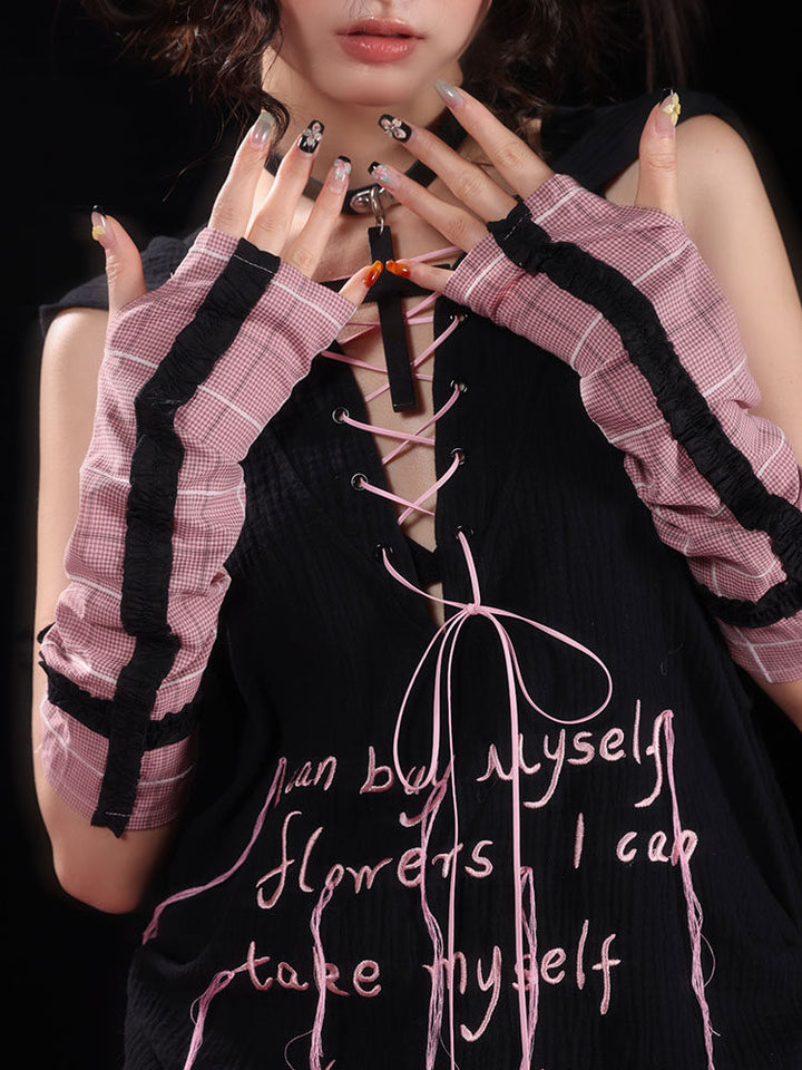 Pink plaid arm warmers cover the forearms and backs of the hands, with black ruffled strips running lengthwise and around the upper cuffs.