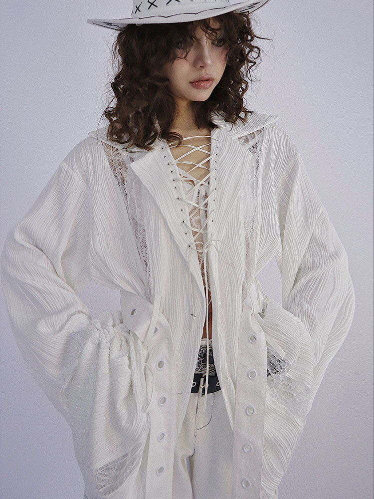 White long-sleeve top with a wide collar framing a deep lace-up opening, gathered sides at the waist, and long grommet straps hanging down the front.