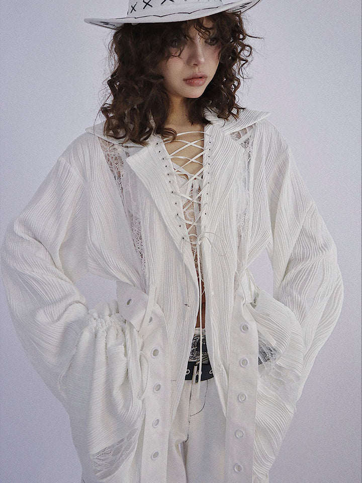 White long-sleeve top with a wide collar framing a deep lace-up opening, gathered sides at the waist, and long grommet straps hanging down the front.