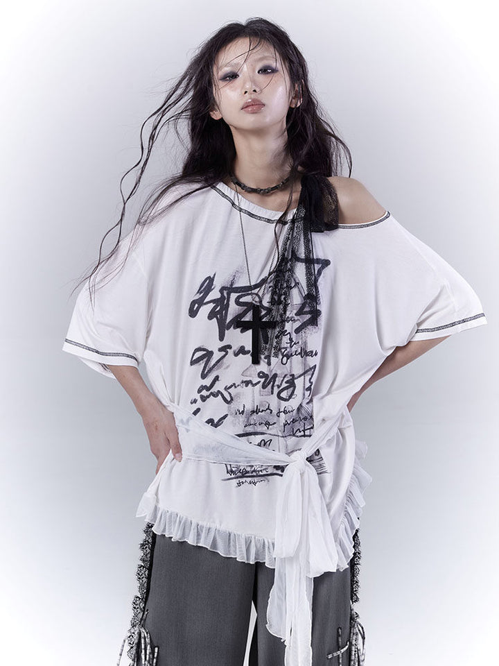 White oversized graphic T-shirt with a wide neckline exposing one shoulder, black lettering across the front and a sheer ruffled hem below a long waist tie.