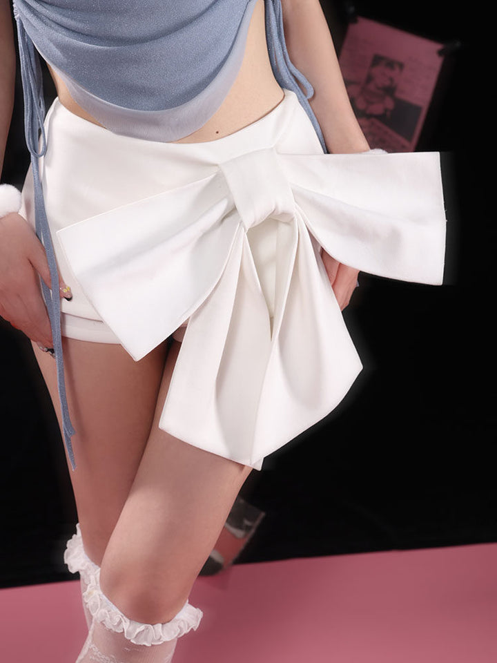 White shorts with an oversized bow across the front, its broad loops spreading over the hips and long tails falling below the hem.